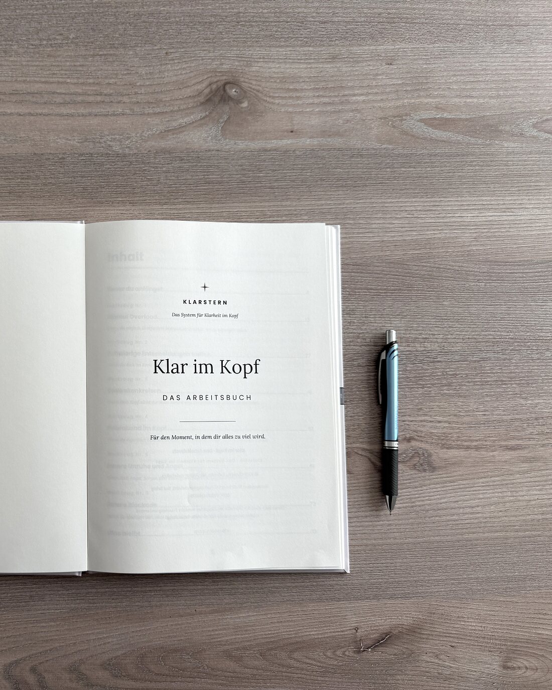 Das aufgeschlagene Arbeitsbuch „Klar im Kopf“ mit Stift und einer Tasse auf einem hellen Holztisch