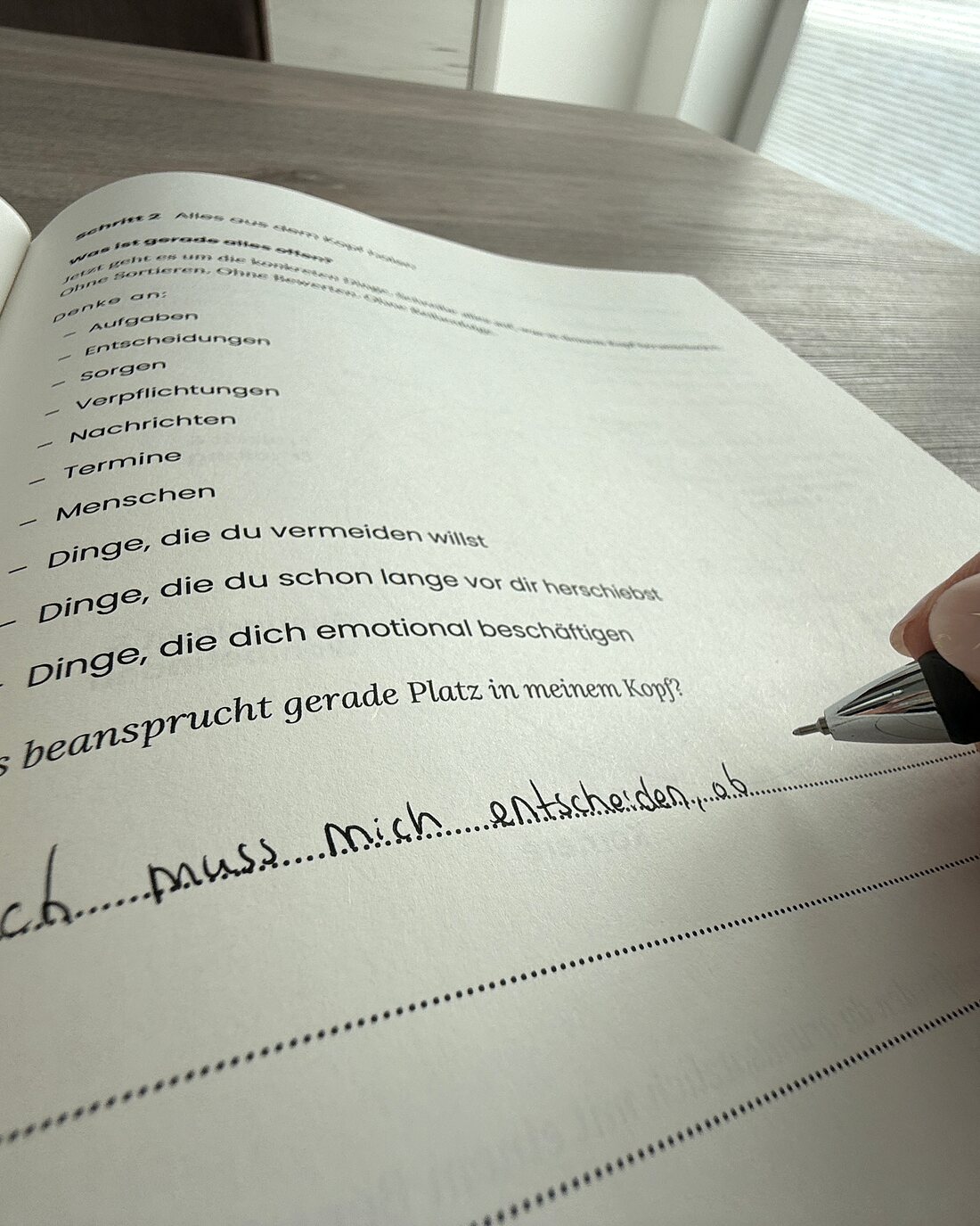 Eine Hand schreibt mit einem Stift in das aufgeschlagene Arbeitsbuch